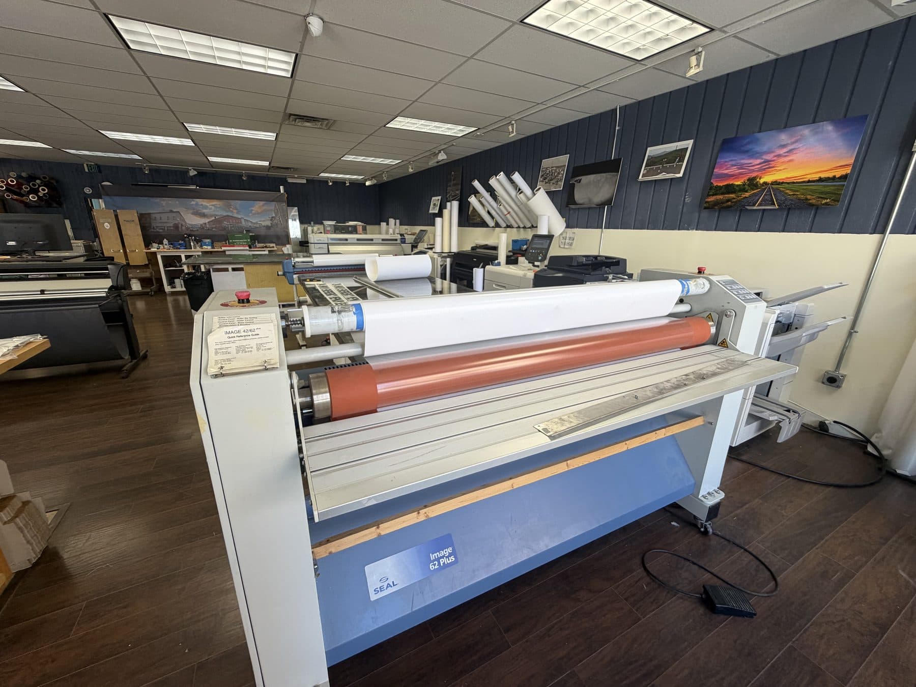 The digital blues shop floor: the wide-format laminator in the foreground, presses along the back wall, and canvas prints hung above them
